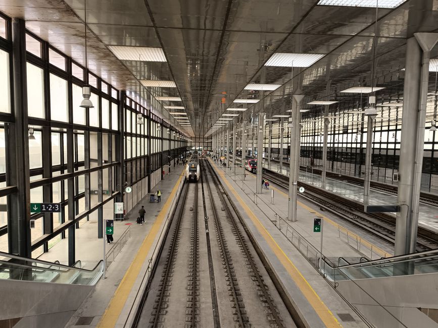A bustling train station in Cádiz with modern architecture and multiple tracks.